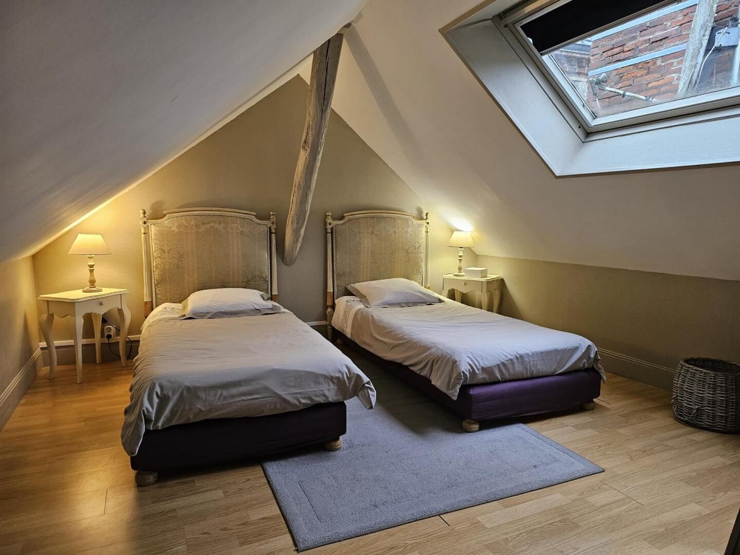 A small, cozy attic bedroom with two single beds, a skylight, and a wooden floor.