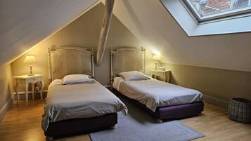 A small, cozy attic bedroom with two single beds, a skylight, and a wooden floor.