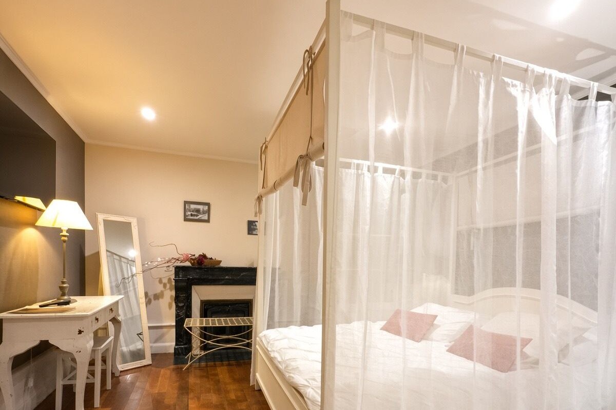 Un dormitorio con cama con dosel, un escritorio con silla, un espejo y una chimenea.