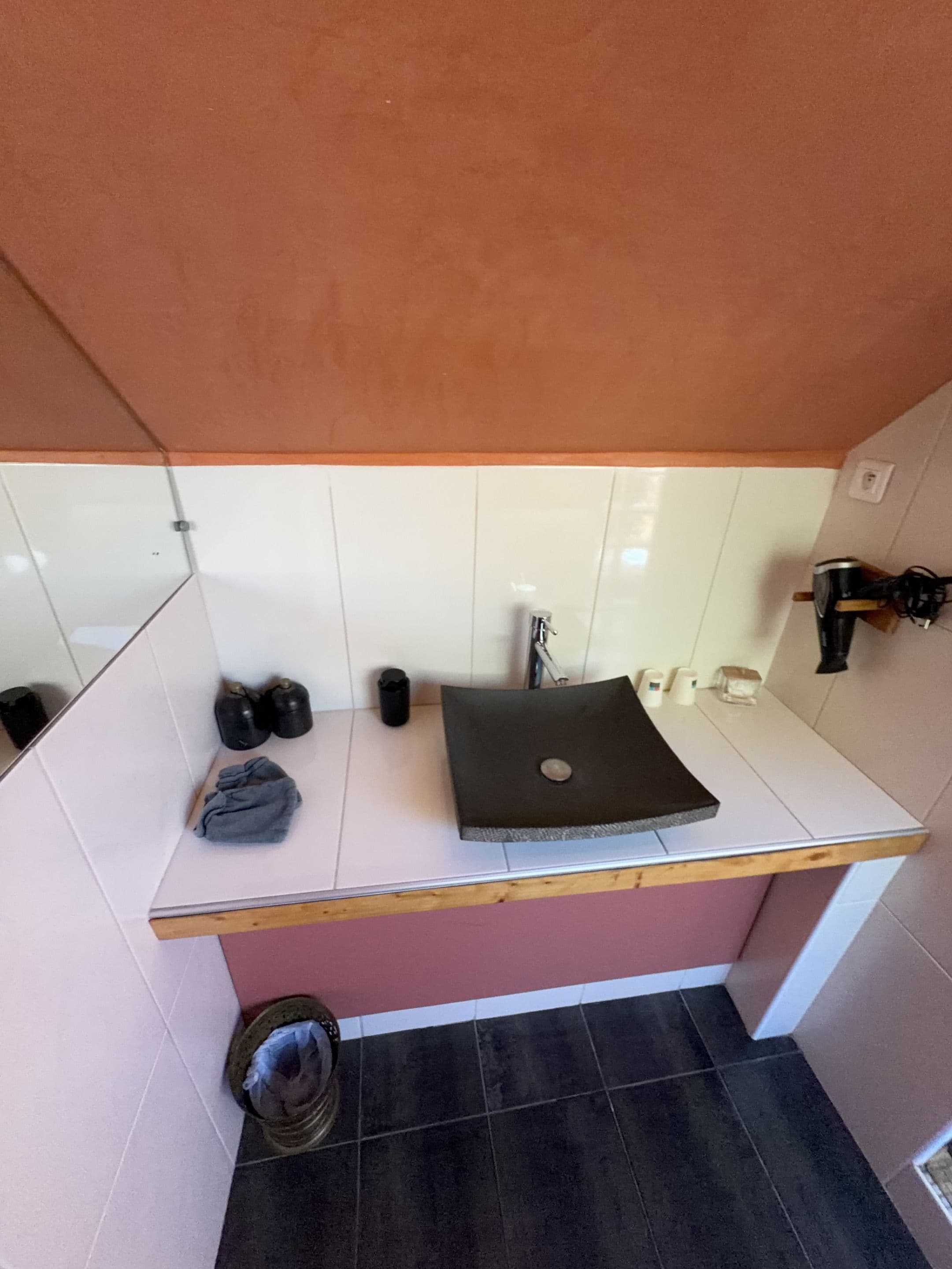 Un bagno con un piano di lavoro bianco, un lavandino nero e uno specchio. Sul piano ci sono scarpe nere e un asciugamano grigio.