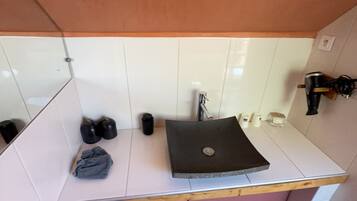 Un bagno con un piano di lavoro bianco, un lavandino nero e uno specchio. Sul piano ci sono scarpe nere e un asciugamano grigio.