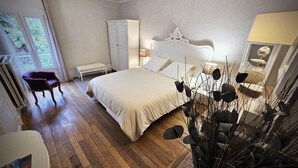 A bedroom with a large bed, a bench, a wardrobe, and a view of greenery outside.