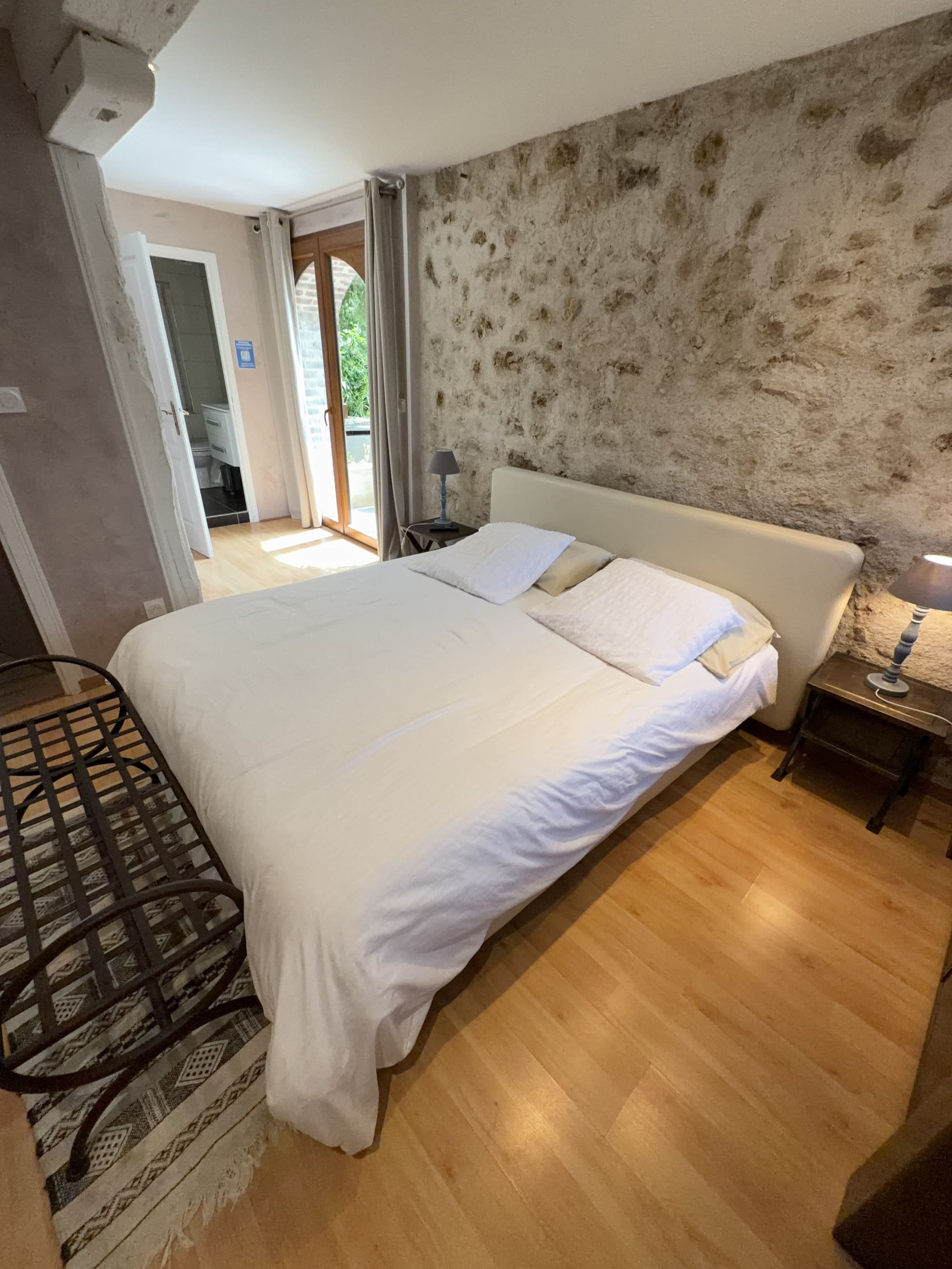 Un dormitorio con cama, mesita de noche, lámpara y vistas al exterior.