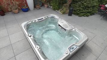 Een bubbelbad in een openlucht setting met betegelde vloer, omringd door potplanten en een rode muur.