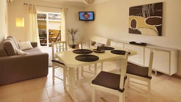 A modern living room with a sofa, dining table, chairs, a TV, and a painting on the wall.