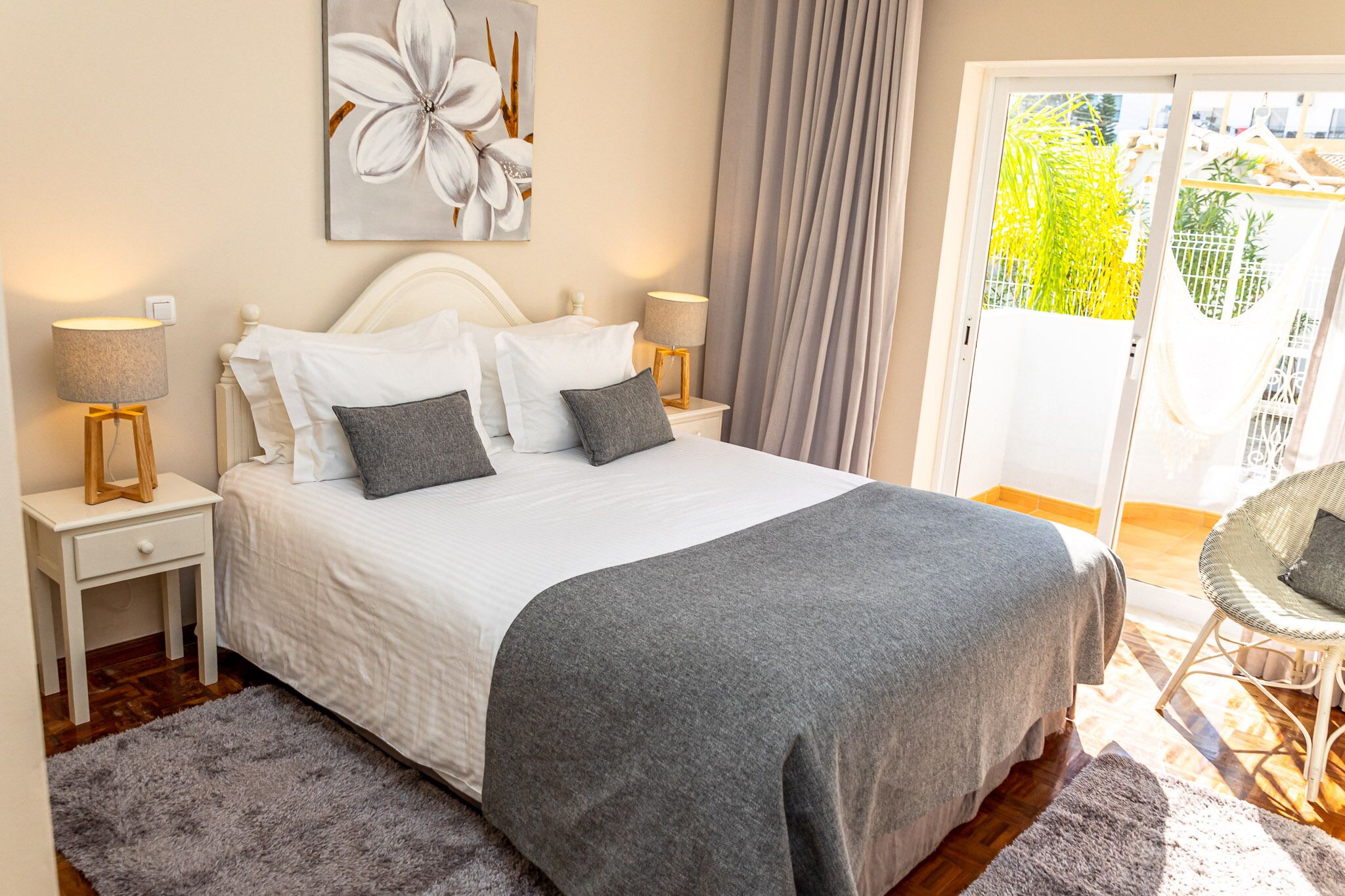 A neatly made bed with a grey blanket, two bedside lamps, and a large floral artwork on the wall.