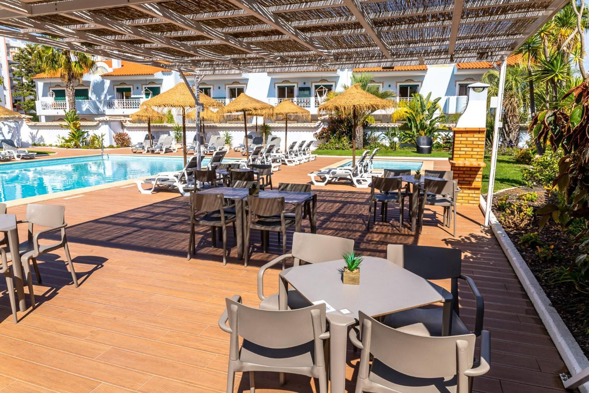 A poolside area with lounge chairs, umbrellas, and a dining table.