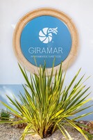 A circular sign with the logo and name 'GIRAMAR APARTAMENTOS TURÍSTICOS' on a blue background, surrounded by a rustic wooden frame.