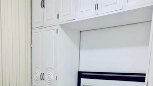 A neatly made bed with white linens, a glass table with a remote control, and white cabinets with decorative handles.