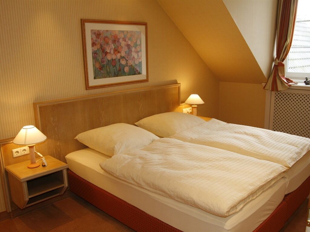 A double bed with two pillows, a wooden headboard, and a nightstand with a lamp.