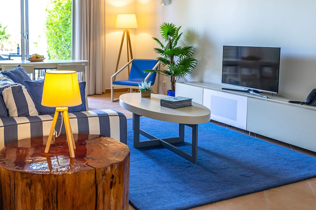 A modern living room with a sofa, a coffee table, a lamp, a TV, and a plant.