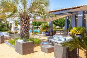 A patio area with wicker furniture, a palm tree, and a pool in the background. - Aldeia Azul (Lagos)