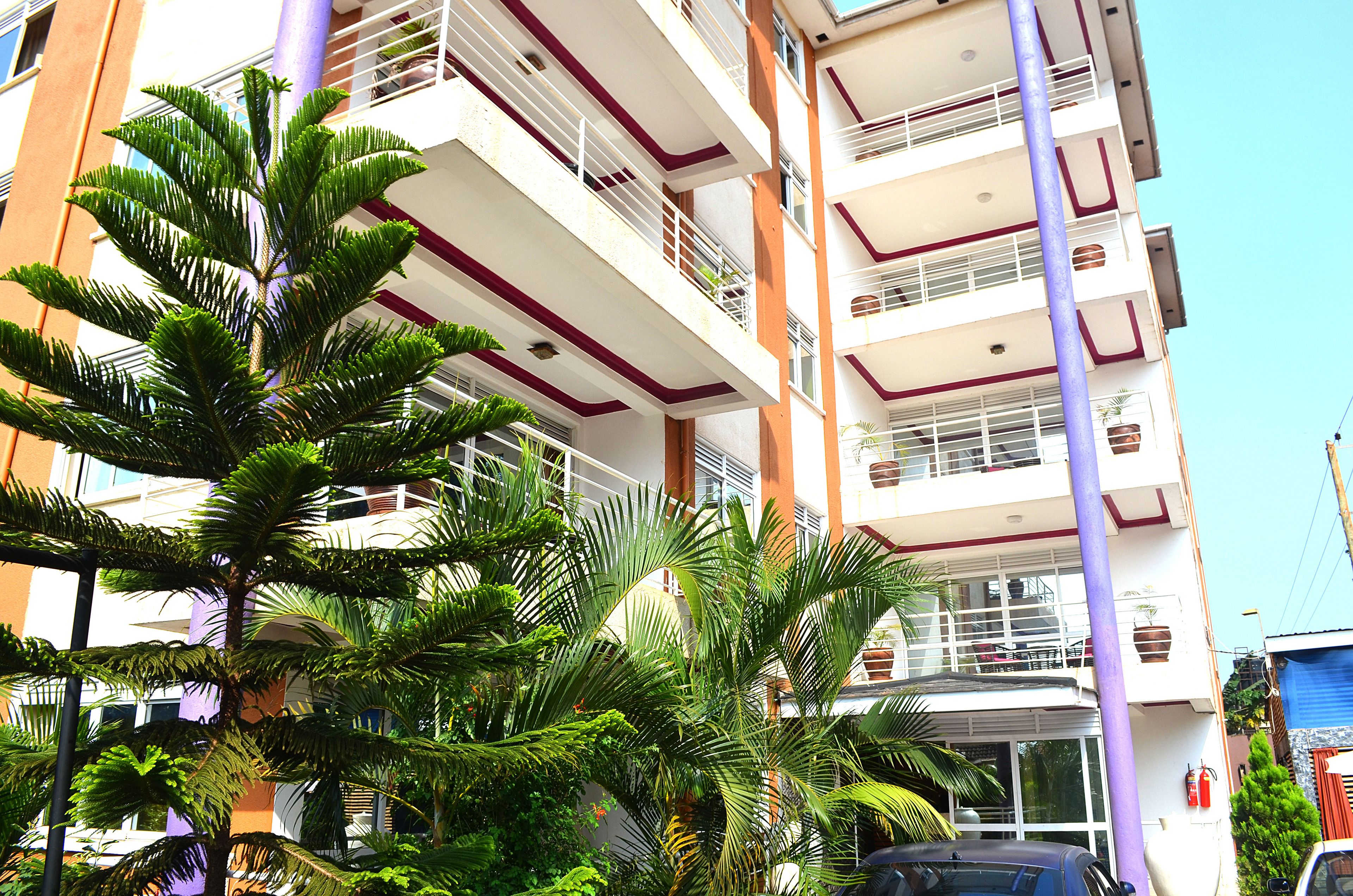 A multi-story building with balconies, a central entrance, and surrounding greenery.