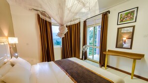 Una habitación de hotel con cama, cortinas, mesita de noche, lámpara y ventana con vistas.