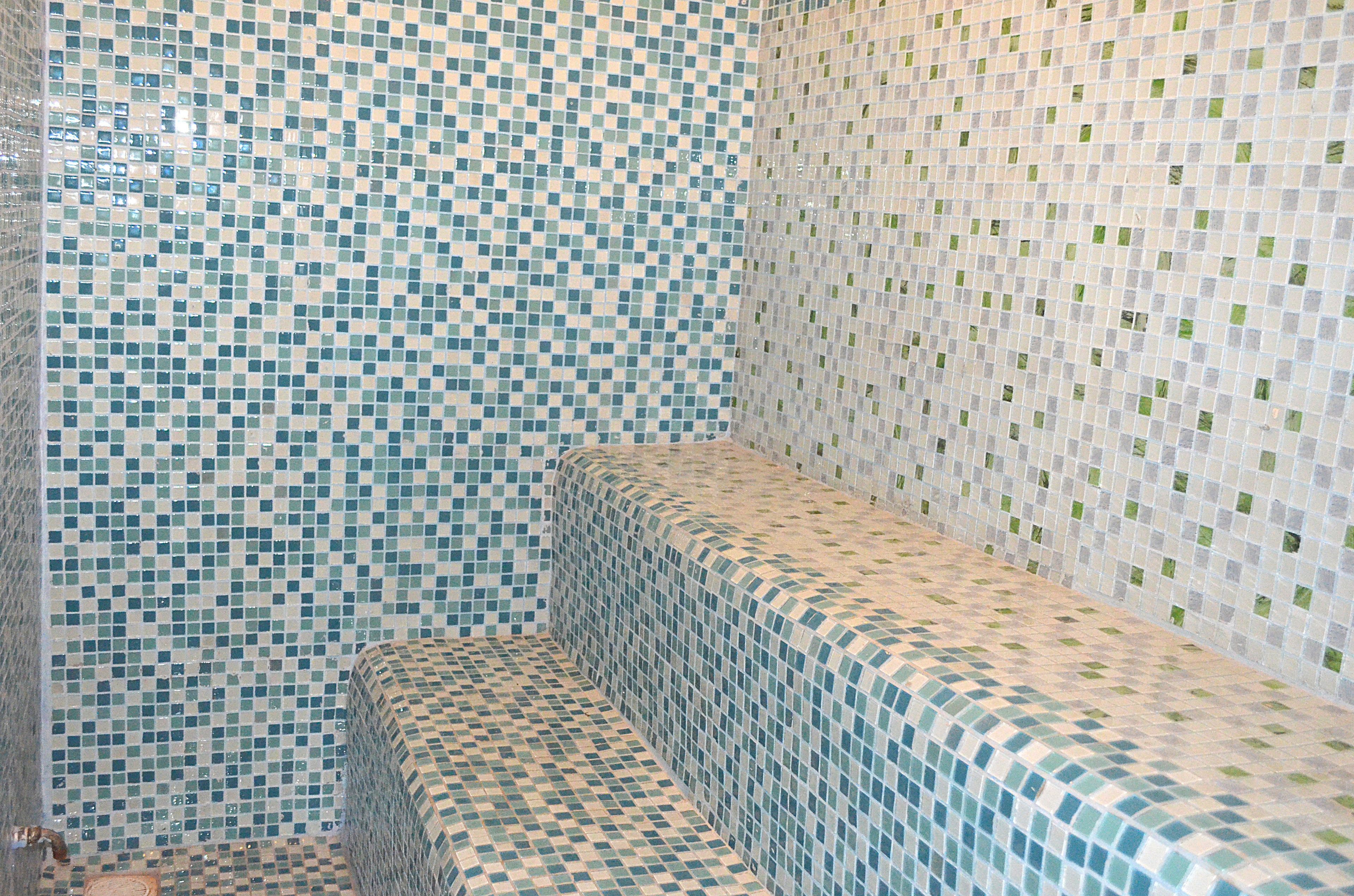 Un baño con paredes de mosaicos y un banco.