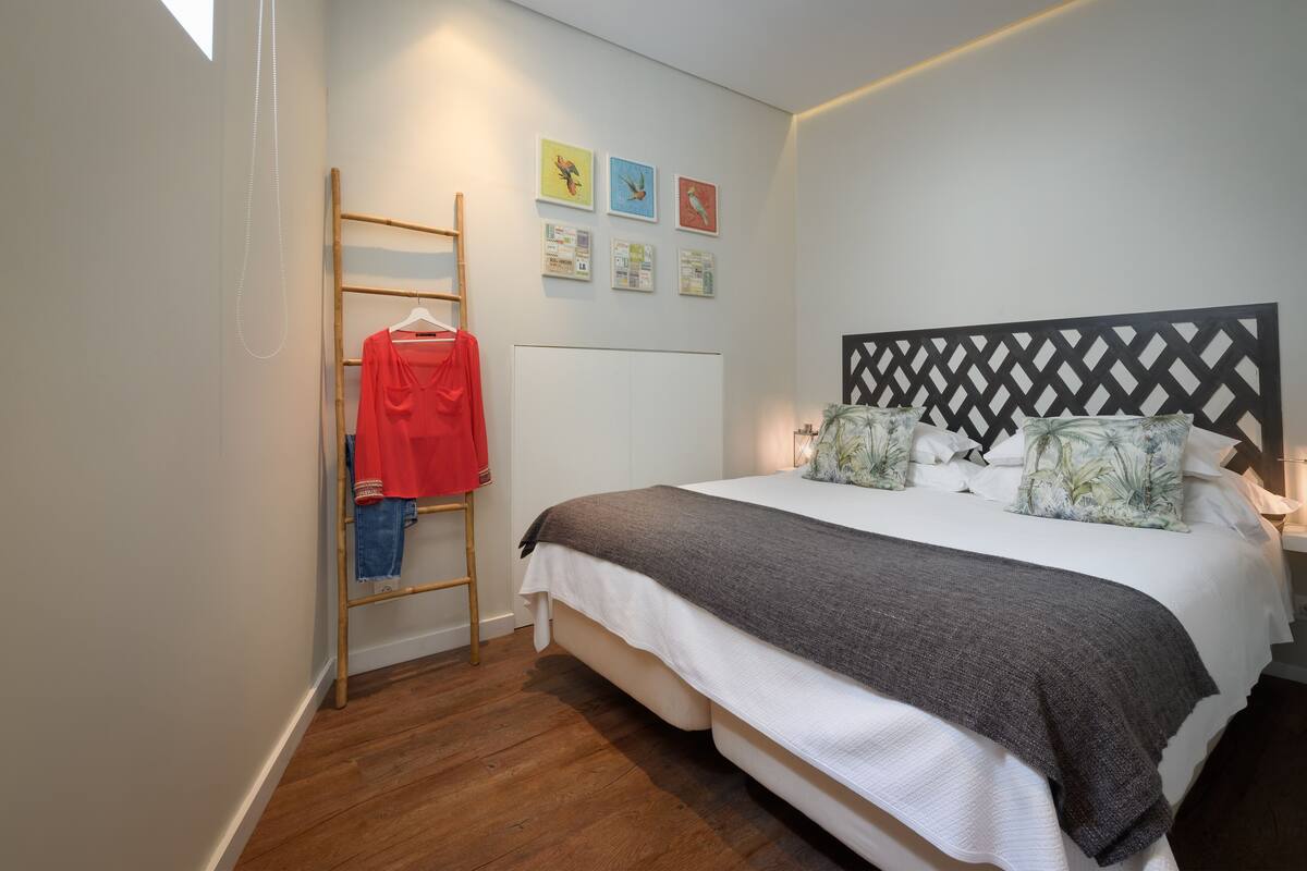 A bedroom with a bed, a wooden ladder, and a wall with framed pictures.