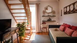 Um quarto moderno com escada de madeira, televisão, planta, cama com almofadas vermelhas e relógio de parede exibindo a hora em diversas cidades.