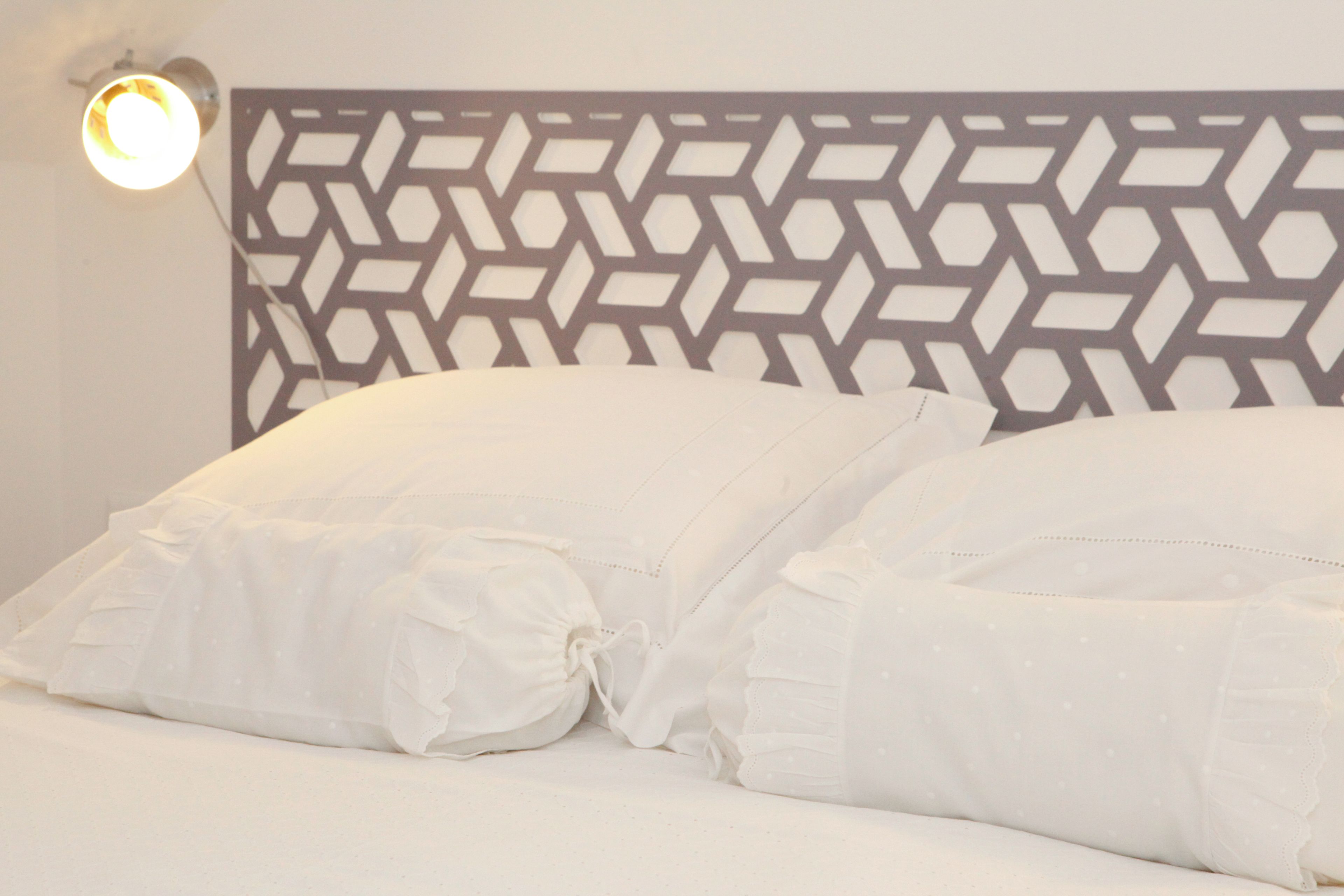 Un lit avec des oreillers blancs et une tête de lit aux motifs géométriques.