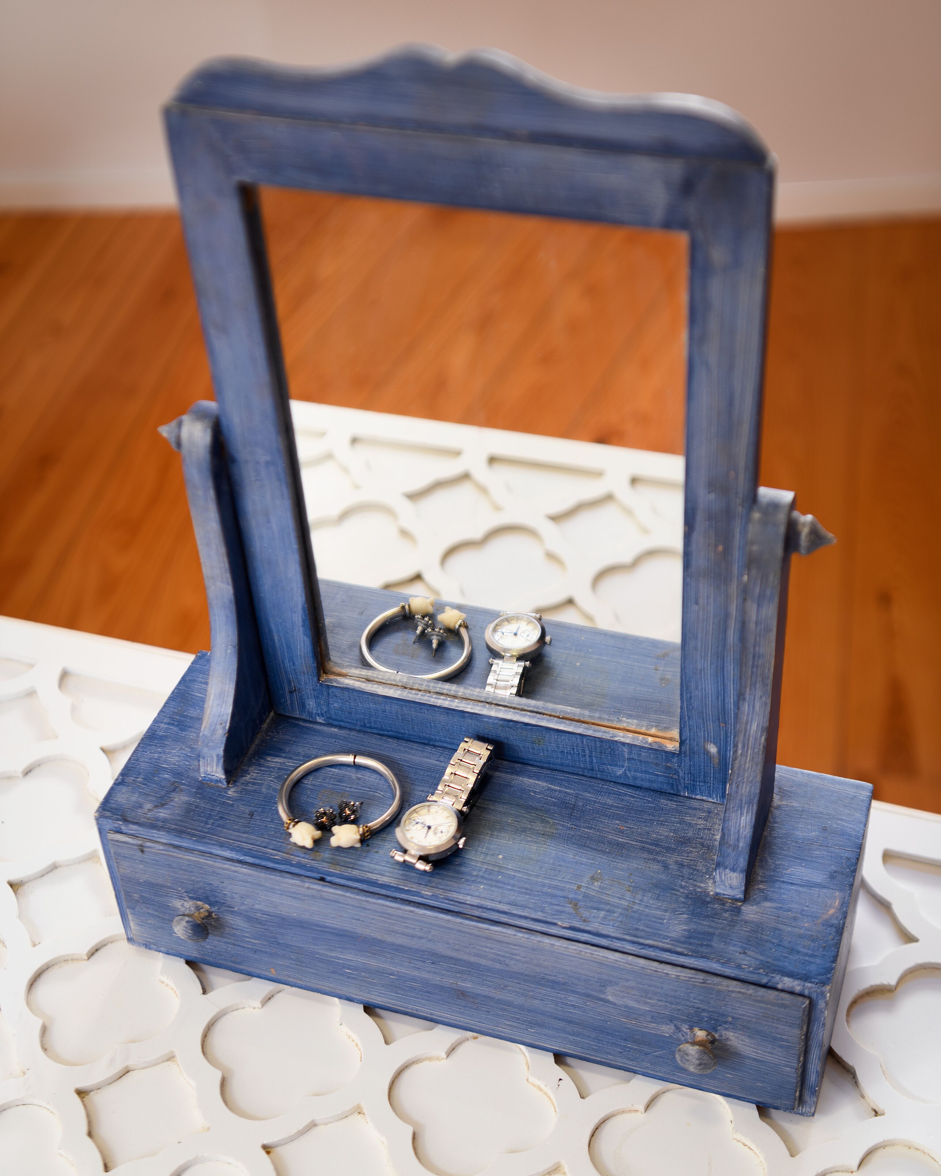 Une petite boîte à bijoux en bois, dotée d’un miroir, contenant des bagues, des bracelets et une montre.