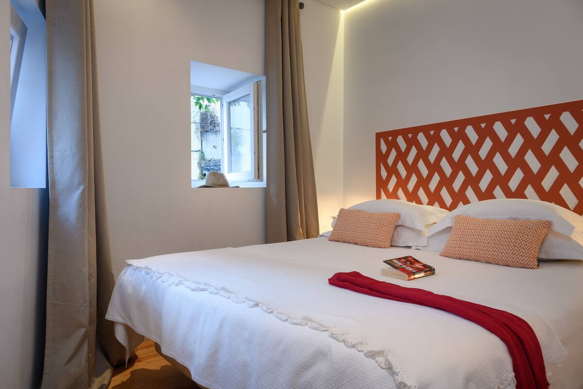 A neatly made bed with a white bedspread, two patterned pillows, and a red throw blanket.