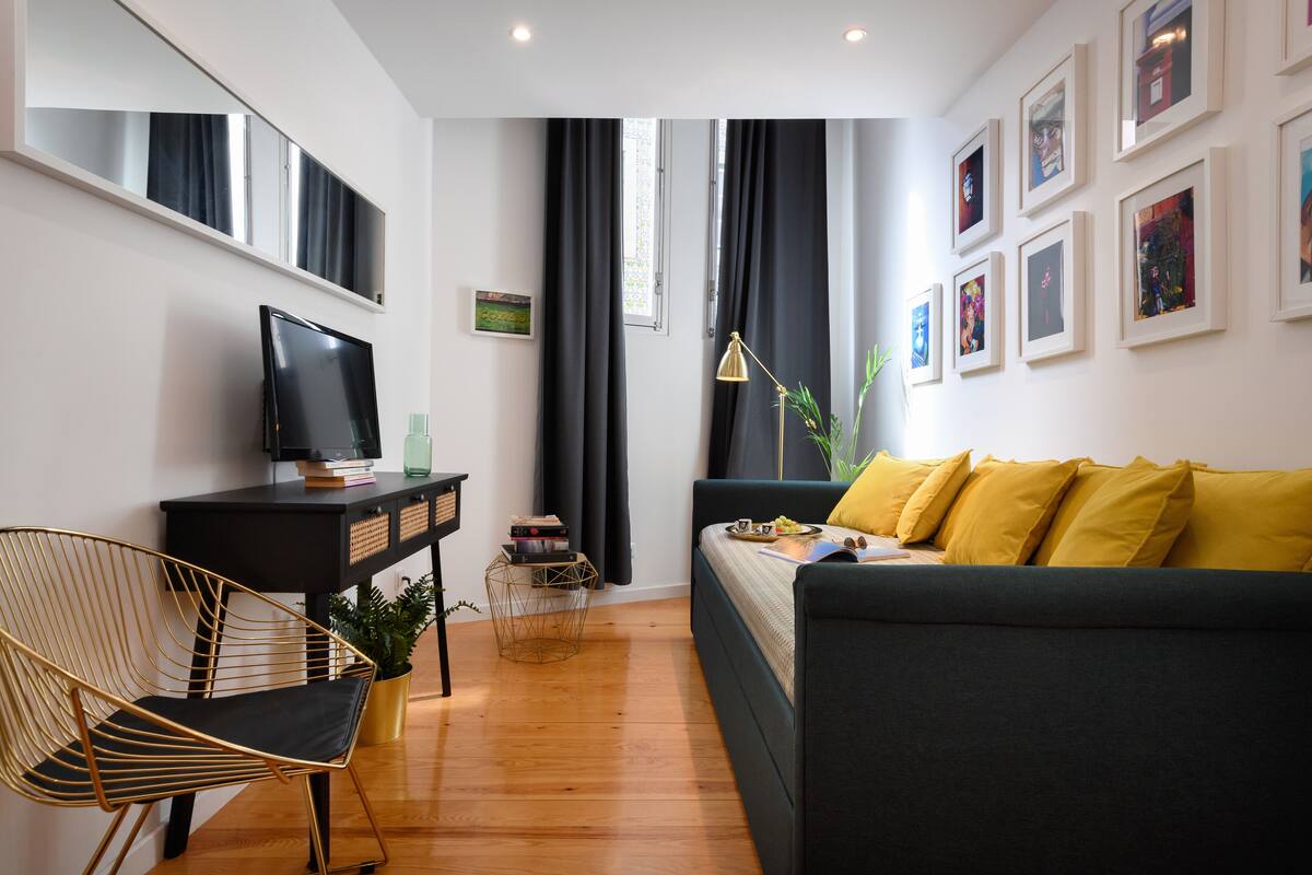 A modern living room with a black sofa, a gold chair, a TV on a black stand, and a plant.