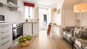 Cozinha moderna com micro-ondas, forno e pia, área de jantar com mesa e cadeiras, e um sofá estampado.
