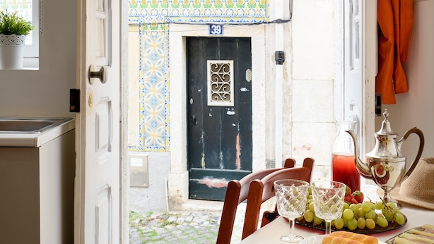 Uma área de refeições com uma mesa posta para dois, uma porta que dá para o exterior e vista para uma parede externa com padrão.