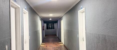 Un largo pasillo con paredes grises, puertas blancas y piso de baldosas.