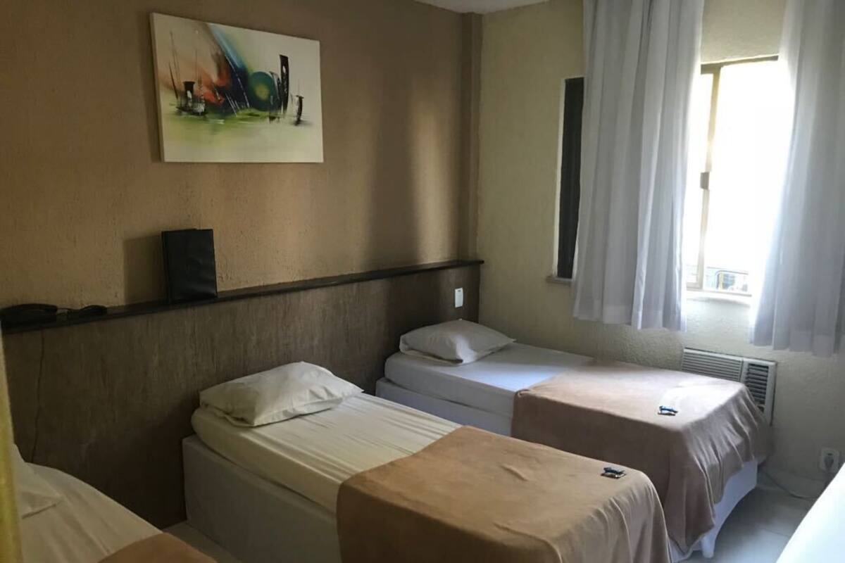 A hotel room with three single beds, a painting on the wall, and a window with curtains.