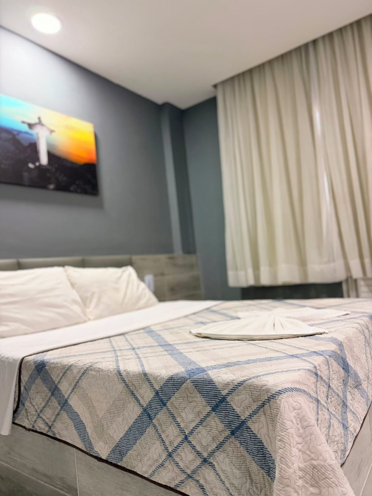 Une chambre d’hôtel avec un lit, un tableau au mur et une fenêtre avec des rideaux.