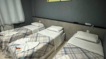 Habitación de hotel con tres camas, cada una con colcha escocesa y almohadas blancas. Un cuadro cuelga en la pared sobre las camas.