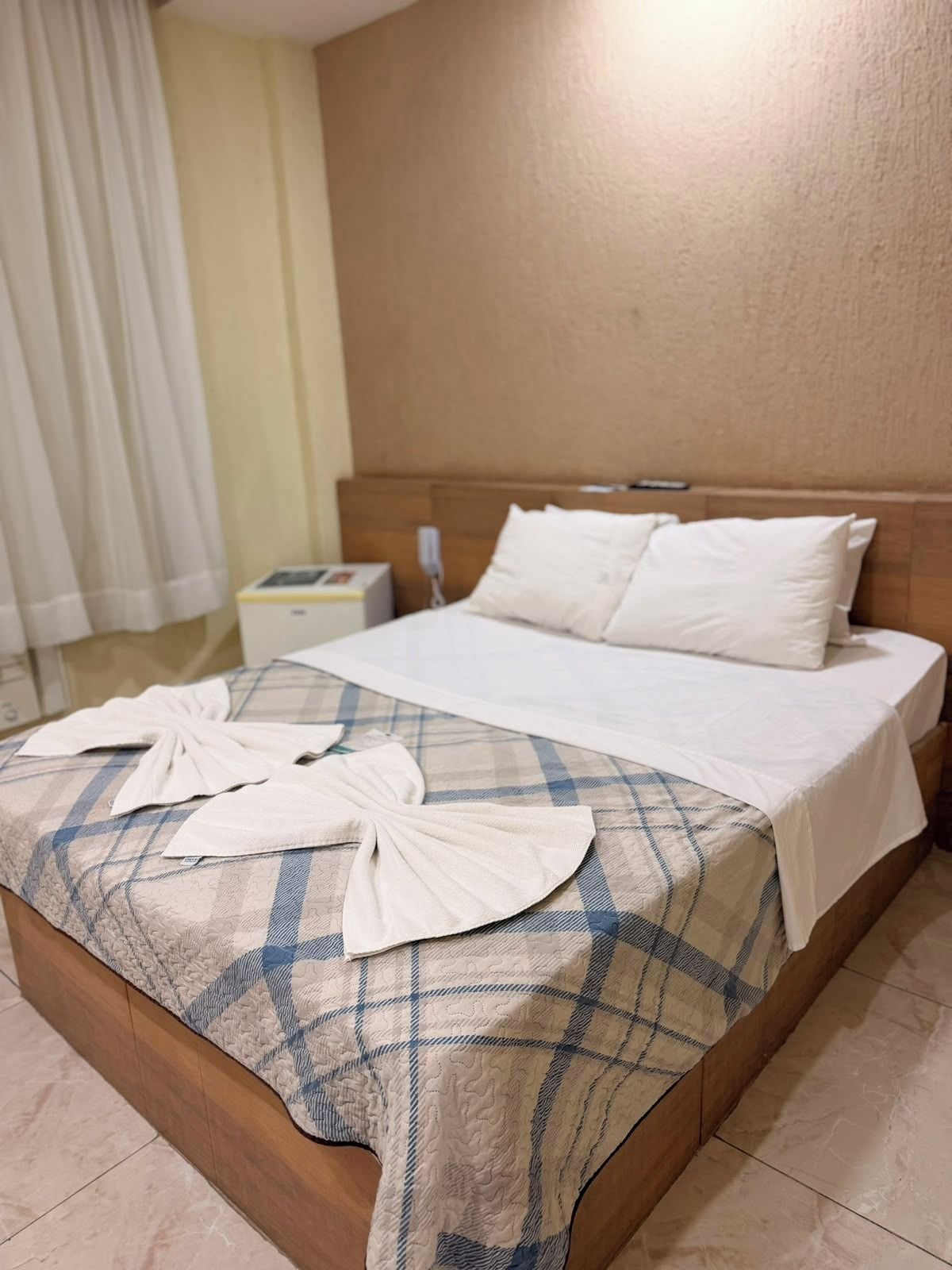 A hotel room with a bed, a nightstand, and a window with curtains.