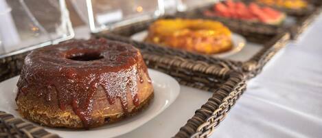 A buffet table with various food items, including a chocolate-glazed donut and a fruit platter.