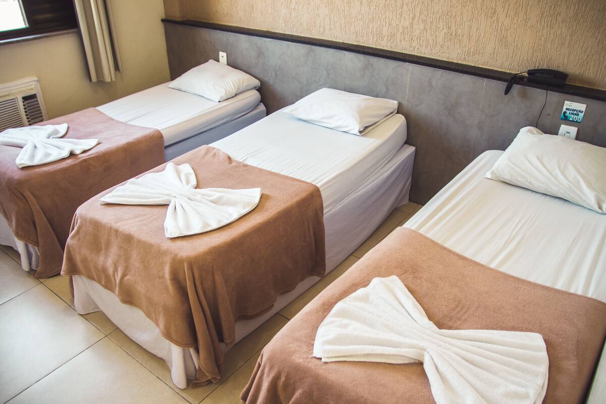 A hotel room with three single beds, each with a brown bedspread and a white towel folded on top.