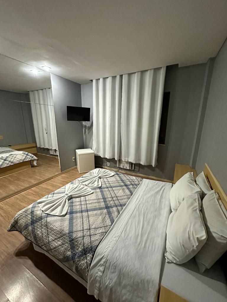 Habitación de hotel con cama, televisor montado en la pared y un espejo que refleja la habitación.