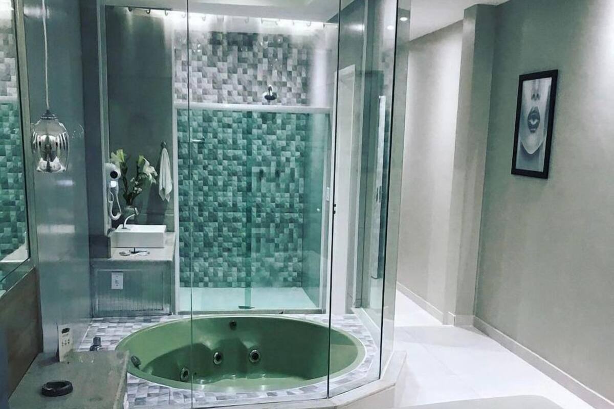 A modern bathroom with a glass-enclosed shower, a freestanding bathtub, and a neatly made bed with towels.