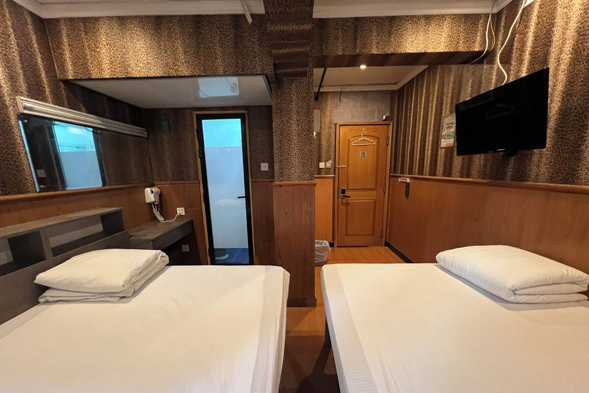 A hotel room with two beds, a TV mounted on the wall, a mirror, and a door leading to a bathroom.