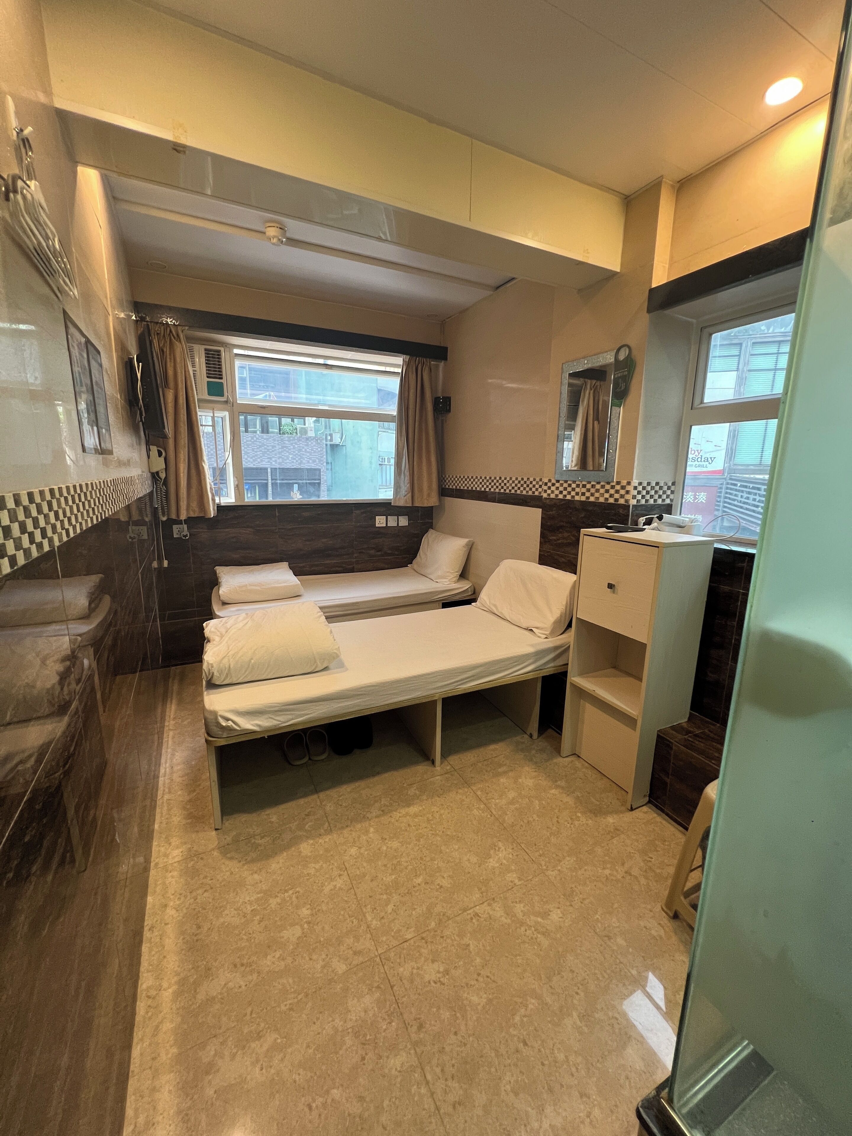 A compact room with a single bed, a small kitchenette, and a window providing a view of the outside.