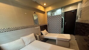 Une chambre d’hôtel avec deux lits, un petit tabouret, un miroir et un rideau de douche à motifs.