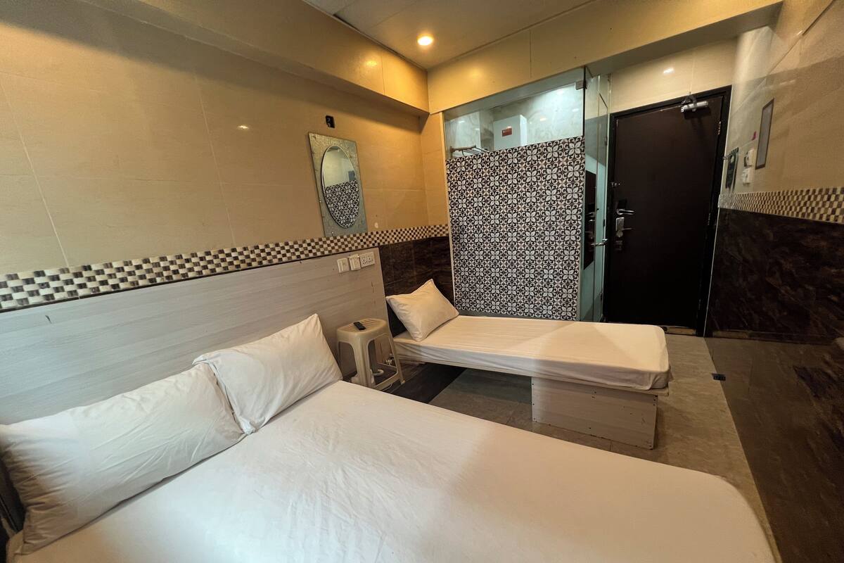 A hotel room with two beds, a small stool, a mirror, and a patterned shower curtain.