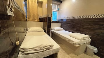 A small, clean room with two single beds, a bathroom with a shower, and a window with blinds.