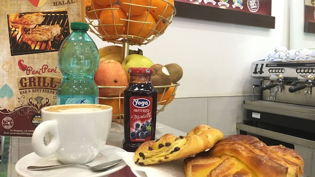 A breakfast setting with a coffee cup, a basket of oranges, a bottle of juice, and pastries. - Wonderful In Rome (Rome)