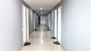 A long, narrow hallway with light blue walls, white doors, and a tiled floor. - Hotel Avenida (São João de Meriti)