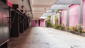 A corridor with a concrete floor, metal railings, and a pink wall with a door at the end. - Hotel Avenida (São João de Meriti)