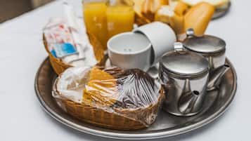 A breakfast tray with a basket, a teapot, a cup, and a glass of orange juice.