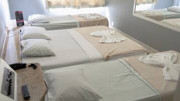 A hotel room with two beds, each with white linens and towels arranged in a bow. A minibar and a control panel are visible on the dresser.