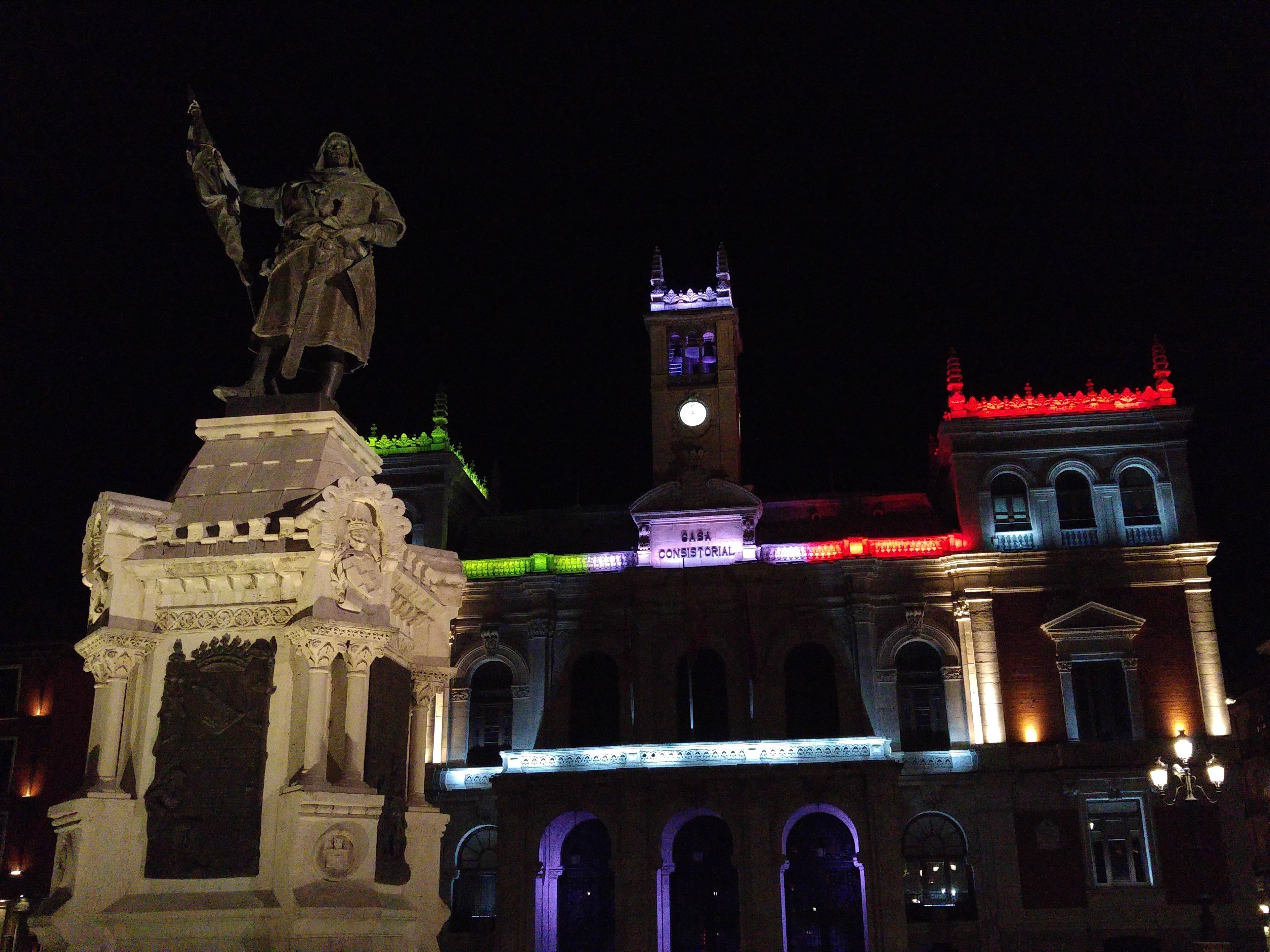 A historical building with a statue on a pedestal, a clock tower, and illuminated facades.