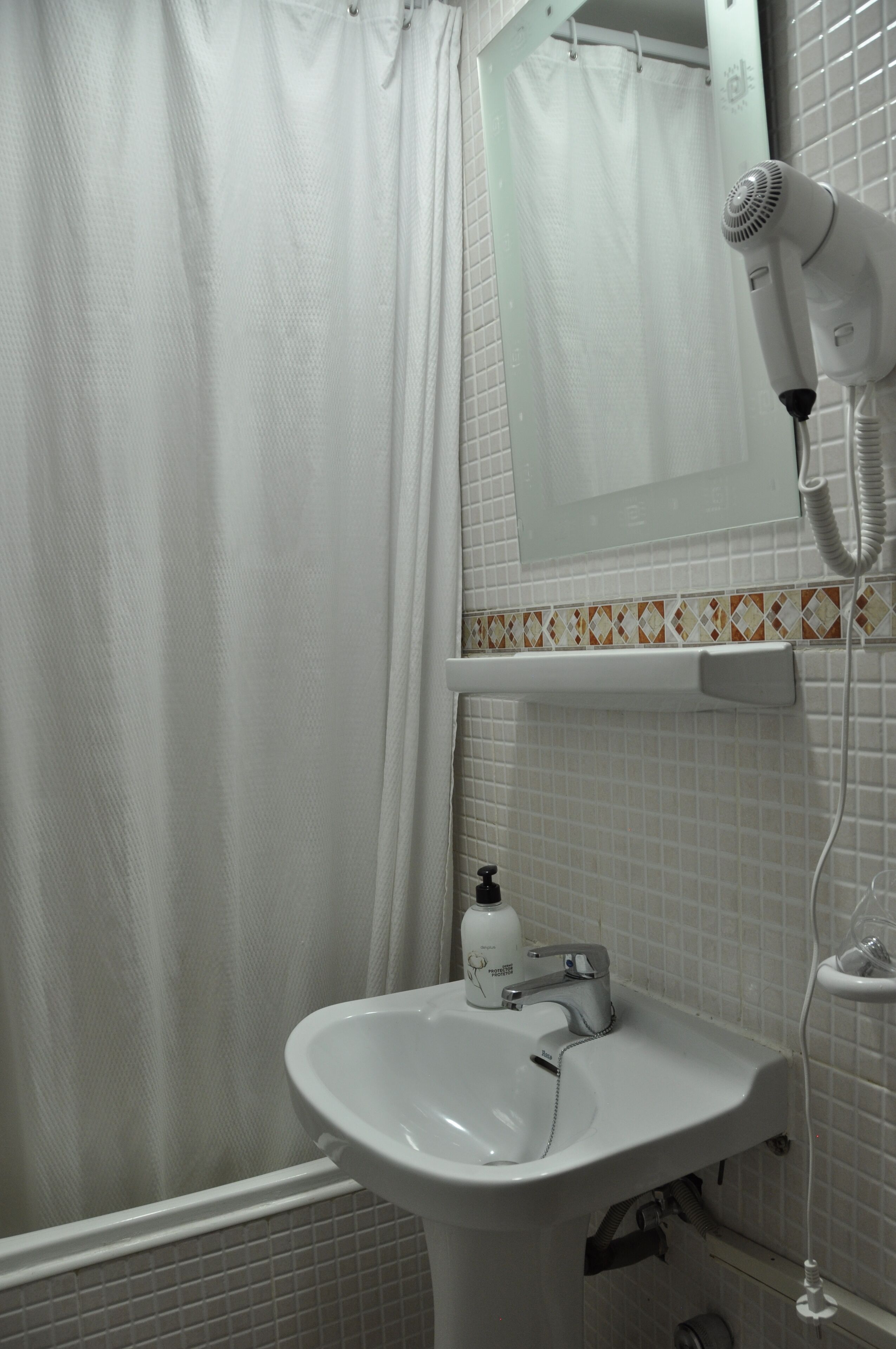 Un baño con lavamanos blanco, espejo, secador de pelo y cortina de ducha.