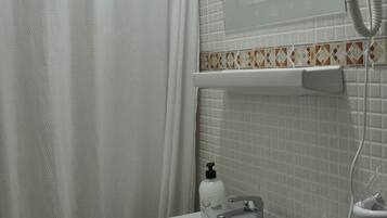 Un baño con lavamanos blanco, espejo, secador de pelo y cortina de ducha.