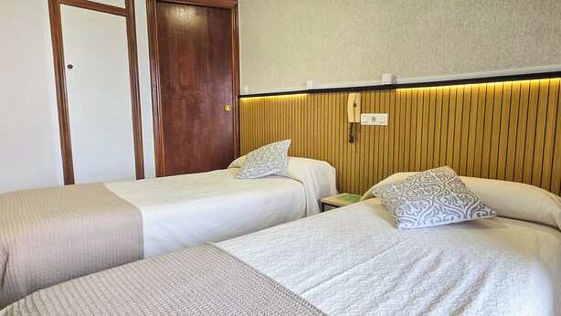 Habitación de hotel con dos camas individuales, un panel de pared de madera, una mesita de noche con lámpara y un teléfono.